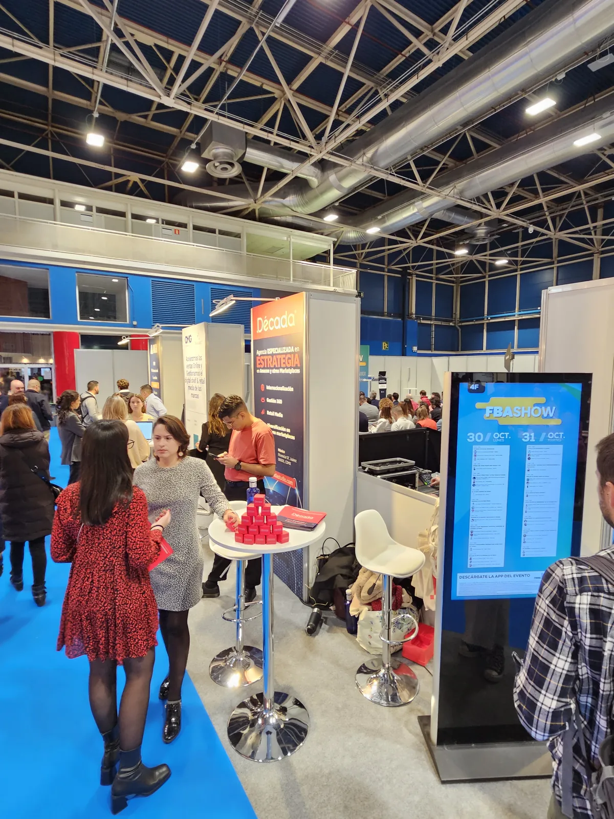 Zona de stands de FBAshow Madrid 2023 con la agenda del día en pantalla